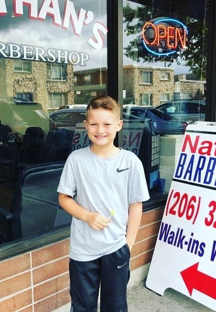Young client outside Nathan's Barbershop on University Way NE, next to the walk-ins sign